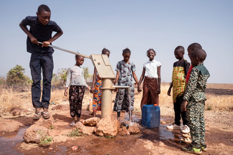 Groupe d enfants autour d une pompe a eau manuelle en zone rurale